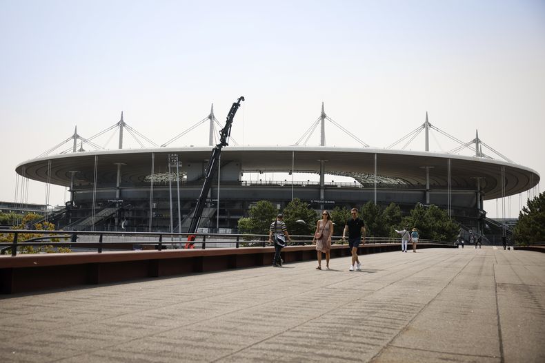 Varias personas caminan cerca del Stade de France, el lunes 10 de julio de 2023, en Saint-Denis. El estadio será la sede del atletismo y el rugby de siete en los Juegos Olímpicos de París de 2024. (AP Foto/Thomas Padilla)