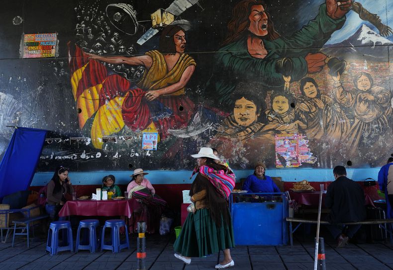 Una mujer camina frente a un mural de temática revolucionaria en El Alto, Bolivia, el miércoles 5 de julio de 2023. Tanto el actual presidente Luis Arce como el expresidente Evo Morales compiten por el control de sindicatos y organizaciones sociales que son la base del gobernante Movimiento al Socialismo (MAS). (AP Foto/Juan Karita)