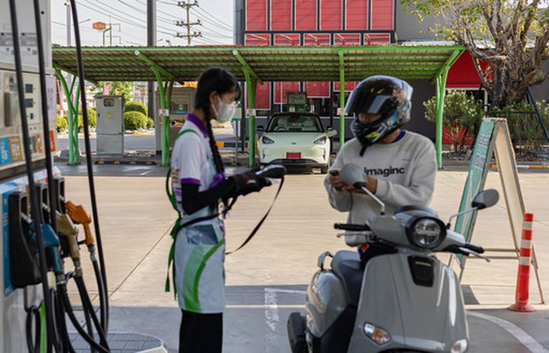 Un motociclista llena el tanque frente a un punto de recarga para vehículos eléctricos en una gasolinera, el 28 de mayo de 2026, en la provincia tailandesa de Nakorn Pathom. (AP Foto/Anton L. Delgado)