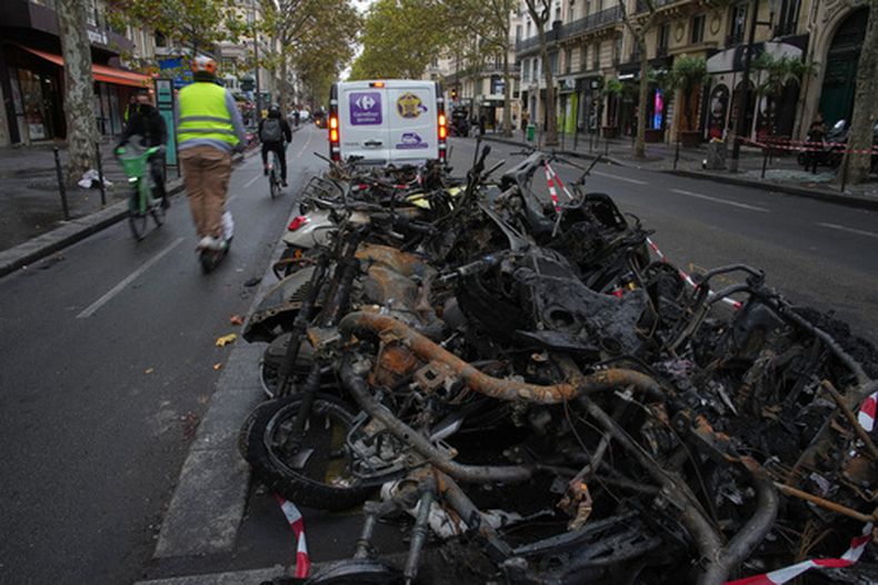 Ciclistas circulan junto a biciletas quemadas tras la primera noche con toque de queda debido a las protestas y disturbios en Paírs el martes 20 de octubre del 2026. (AP Foto/Christophe Ena)