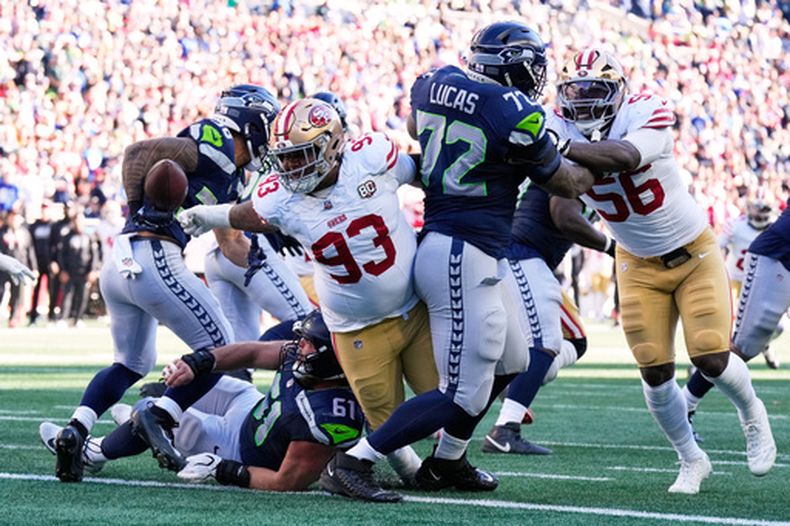 Gracen Halton (93), tackle defensivo de los 49ers de San Francisco, le arranca el balón a George Holani (36), corredor de los Seahawks de Seattle, durante la primera mitad del partido de la NFL, el domingo 11 de octubre de 2026, en Seattle. (AP Foto/Stephen Brashear)