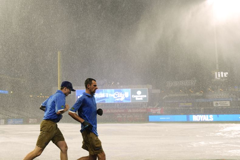 Un par de trabajadores coloca la lona para cubrir el terreno durante un aguacero en el juego del martes 2 de julio de 2024, entre los Reales de Kansas City y los Rays de Tampa Bay (AP Foto/Charlie Riedel)