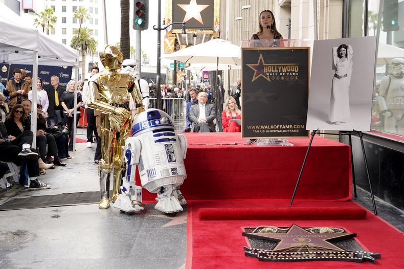 Billie Lourd habla durante una ceremonia en honor a su madre, la fallecida actriz Carrie Fisher, que aparece en una fotografía a la derecha, al develar una estrella póstuma en el Paseo de la Fama de Hollywood junto a los personajes de Star Wars C-3PO y R2-D2 en Los Ángeles el jueves 4 de mayo de 2023. La fecha se conoce también como Día de Star Wars, en homenaje a las películas de Star Wars en las que Fisher interpretó a la Princesa Leia. STAR WARS-CARRIE FISHER