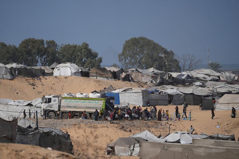 Palestinos desplazados se reúnen para llenar recipientes de agua de un proveedor en Deir al-Balah, en el centro de la Franja de Gaza, el sábado 10 de octubre de 2026. (AP Foto/Abdel Kareem Hana)