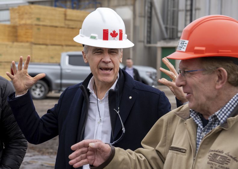 El primer ministro canadiense, Mark Carney, bromea sobre su casco con el presidente de Elmsdale Lumber Yard, Robin Wilber, en un evento de campaña en el aserradero, en Elmsdale, Nueva Escocia, el martes 25 de marzo de 2025. (Frank Gunn/The Canadian Press vía AP)