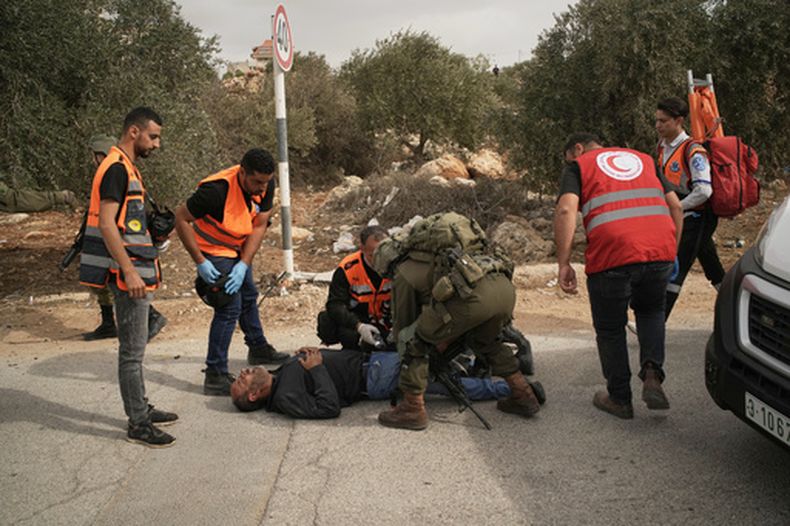 Médicos palestinos y un soldado israelí atienden a un hombre palestino baleado por soldados israelíes tras un ataque de colonos a palestinos que cosechaban aceitunas en el pueblo de Abu Falah, Cisjordania, el viernes 16 de octubre de 2026. (AP Foto/Leo Correa)