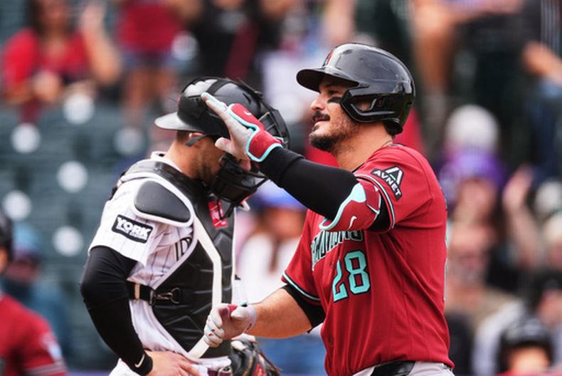 El pelotero de los Diamondbacks de Arizona, Nolan Arenado (frente), hace gestos mientras cruza el plato tras conectar un cuadrangular de dos carreras, mientras el receptor de los Rockies de Colorado, Brett Sullivan, espera que se reanude el juego en la primera entrada de un partido de béisbol, el jueves 24 de septiembre de 2026, en Denver. (Foto AP/David Zalubowski)