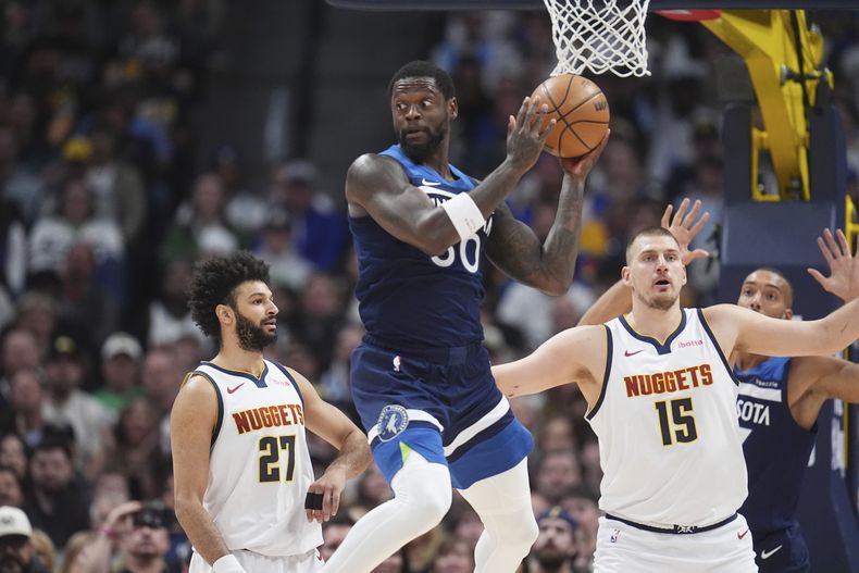 El alero de los Timberwolves de Minnesota Julius Randle intenta pasar el balón frente a Jamal Murray y Nikola Jokic de los Nuggets de Denver el miércoles 12 de marzo del 2025. (AP Foto/David Zalubowski)