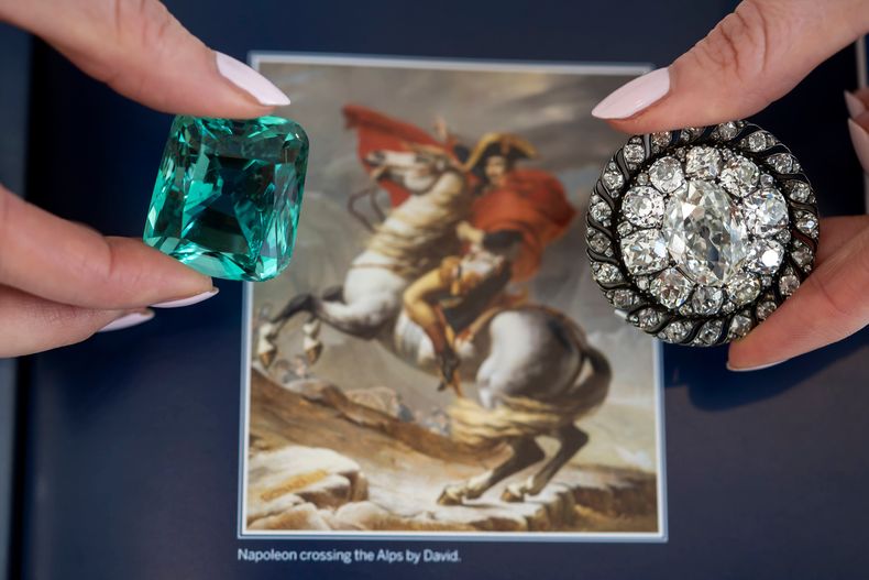 Una empleada de Sothebys muestra un berilo verde, de más de 132 quilates, que se dice que Napoleón usó en su coronación de 1804, y un broche de diamantes que alguna vez fue propiedad del emperador, en Sothebys en Ginebra, Suiza, el jueves 6 de noviembre de 2025. (Martial Trezzini/Keystone vía AP)