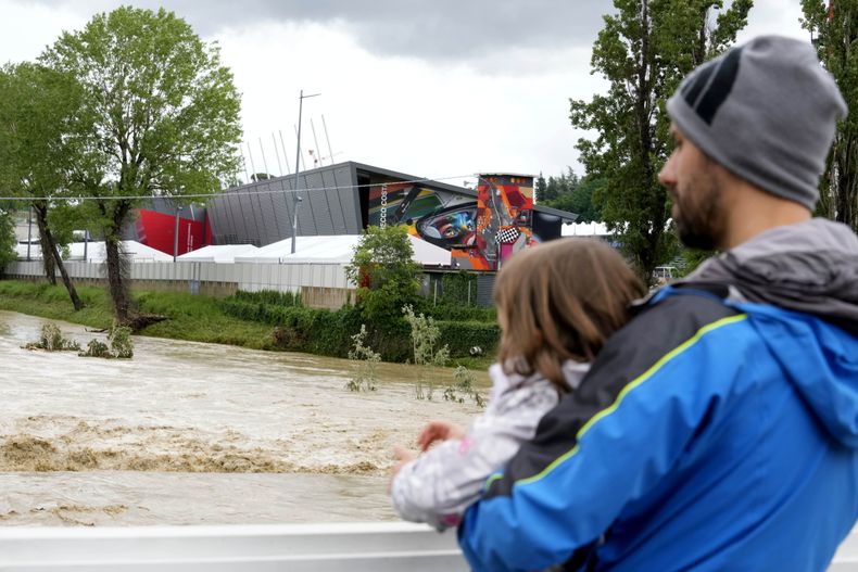 Un hombre con un niño en brazos contempla la crecida del río Santerno, y en el fondo de ve el circuito Enzo e Dino Ferrari en Imola, Italia, 17 de mayo de 2023. Las inundaciones en la región han obligado a cancelar el Gran Premio de Fórmula Uno de la Emilia Romagna, que se debía correr en Imola el próximo fin de semana. (AP Foto/Luca Bruno)