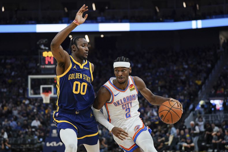 Shai Gilgeous-Alexander, del Thunder de Oklahoma City, avanza hacia la cesta junto a Jonathan Kuminga, de los Warriors de Golden State, el jueves 16 de noviembre de 2023 (AP Foto/Loren Elliott)