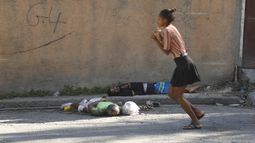 Una mujer pasa junto a los cuerpos de dos hombres asesinados por agresores desconocidos, el domingo 3 de marzo de 2024, en Puerto Príncipe, Haití. (AP Foto/Odelyn Joseph)