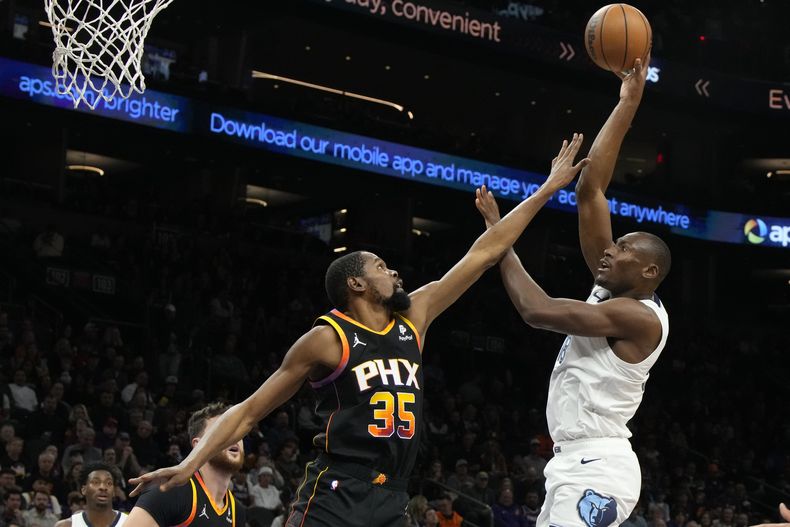 Bismack Biyombo de los Grizzlies de Memphis dispara al aro ante Kevin Durant de los Suns de Phoenix, el sábado 2 de diciembre de 2023, en Phoenix. (AP Foto/Rick Scuteri)