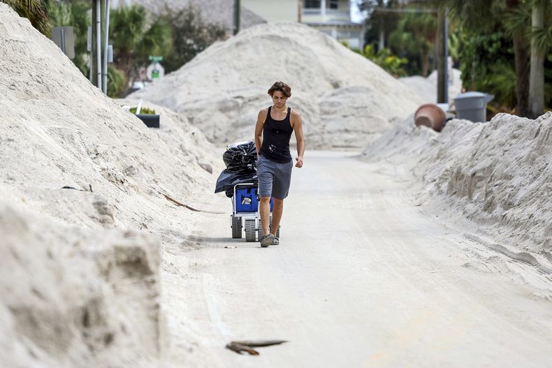 David DeMeza camina con sus pertenencias entre calles cubiertas de arena arrastrada por el huracán Helene, el 2 de octubre de 2024, en Treasure Island, Florida (AP Foto/Mike Carlson)