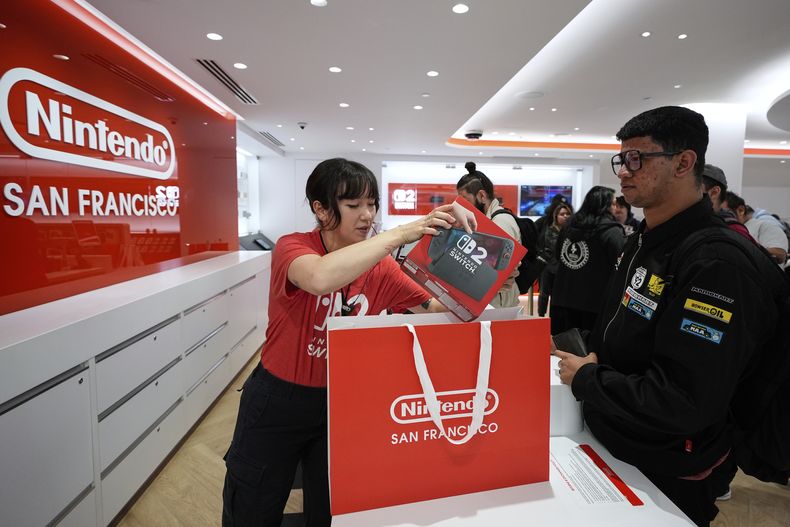 La embajadora especialista de Nintendo, Cyan Chang, a la izquierda, coloca una consola Nintendo Switch 2 dentro de una bolsa para Ronald Diaz, el jueves 5 de junio de 2025, en San Francisco. (AP Foto/Godofredo A. Vásquez)