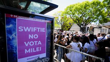 Fanáticos de Taylor Swift esperan en la entrada del Estadio Monumental donde la cantante dará su primer concierto de The Eras Tour, en Buenos Aires, Argentina, frente a un cartel que se refiere al candidato presidencial Javier Milei, el jueves 9 de noviembre de 2023. (AP Foto/Natacha Pisarenko)