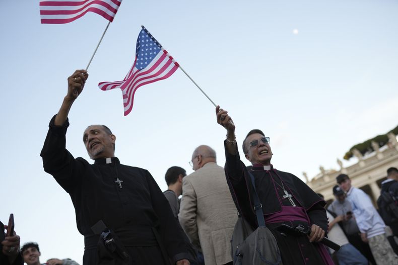 Dos clérigos ondean banderas de Estados Unidos durante el discurso del recién elegido papa León XIV, el jueves 8 de mayo de 2025, en el Vaticano. (AP Foto/Francisco Seco)