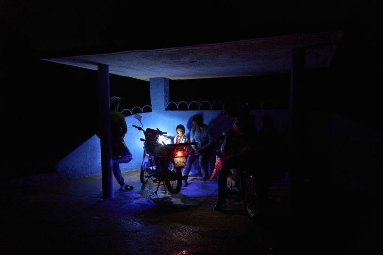Unas personas esperando el autobús iluminadas por el faro de una motocicleta en un corte parcial de luz en La Gallega, en La Habana, Cuba, el domingo 1 de junio de 2025. (AP Foto/Ramón Espinosa)