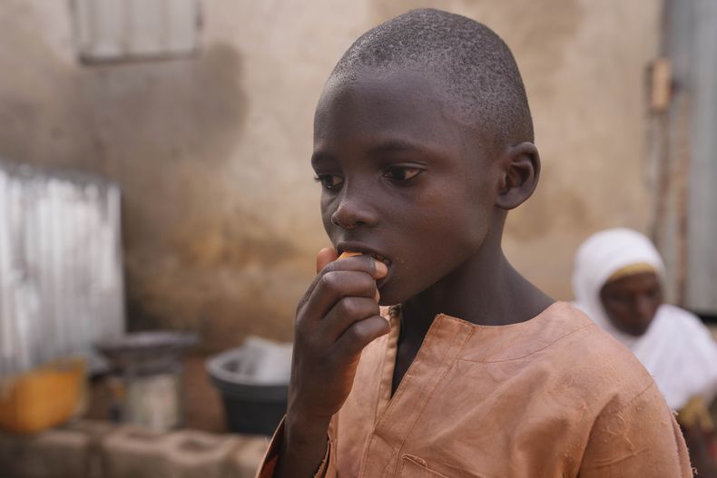 ARCHIVO - Suleiman, nieto de Hauwa Bwami, come un boniato de pulpa anaranjada cosechado en su granja de Kaltungo Poshereng, Nigeria, el domingo 2 de junio de 2024. (AP foto/Sunday Alamba, archivo)
