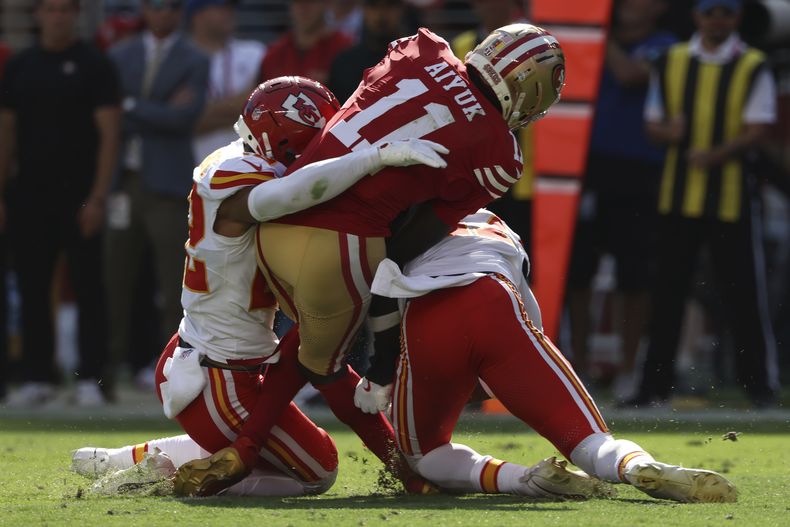 Brandon Aiyuk (11), wide receiver de los 49ers de San Francisco, recibe un golpe de Trent McDuffie, izquierda, y Chamarri Conner, de los Chiefs de Kansas City, durante la primera mitad del juego de la NFL en Santa Clara, California, el domingo 20 de octubre de 2024. (AP Foto/Jed Jacobsohn)