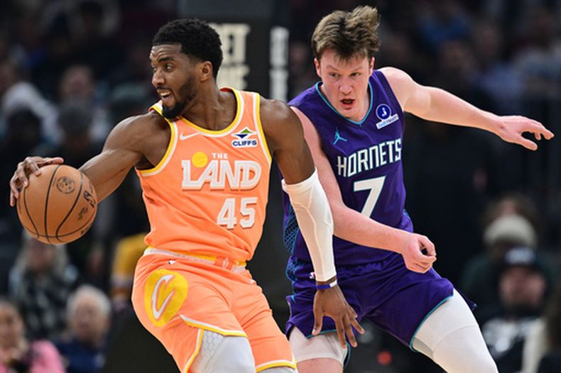 El base de los Cavaliers de Cleveland Donovan Mitchell da una giro con el balón frente al base de los Hornets de Charlotte Kon Knueppel en el encuentro del lunes 22 de diciembre del 2025. (AP Foto/David Dermer)