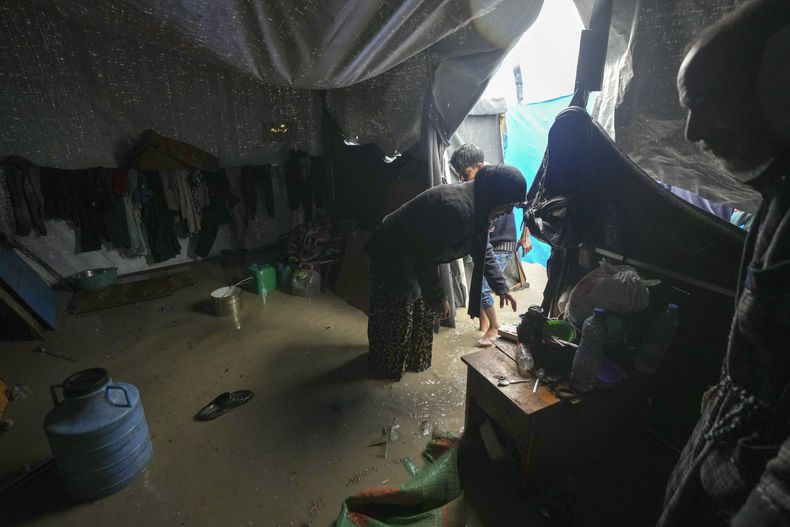 Manal Lubbad, de 49 años, madre de ocho hijos y desplazada desde Ciudad de Gaza, intenta limpiar su carpa inundada tras fuertes lluvias durante la noche en el campamento para refugiados en Deir al Balah, en el centro de la Franja de Gaza, el martes 31 de diciembre de 2024. (AP Foto/Abdel Kareem Hana)
