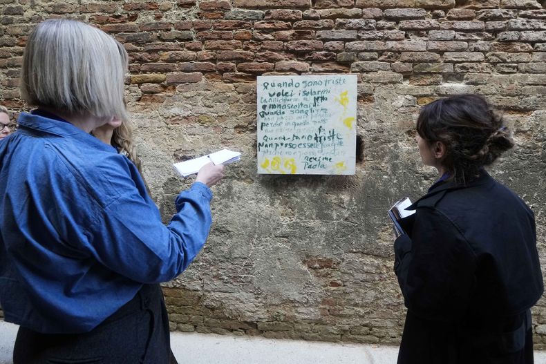 Reporteras observan una instalación de la artista Corita Kent exhibida dentro de la prisión de mujeres en la isla Giudecca durante la exposición de la 60a Bienal de Artes en Venecia, Italia, el miércoles 17 de abril de 2024. La obra forma parte del pabellón del Vaticano en la Bienal de Venecia en una colaboración innovadora entre reclusas y artistas. (Foto AP/Luca Bruno)
