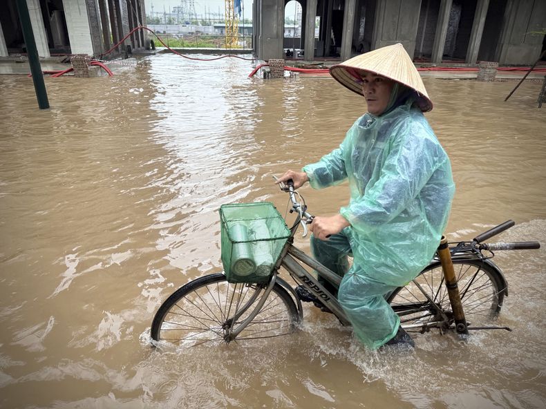 Un hombre monta en bicicleta en una calle inundada por el tifón Kajiki en Hanói, Vietnam, el miércoles 27 de agosto de 2025. (AP Foto/Hau Dinh)