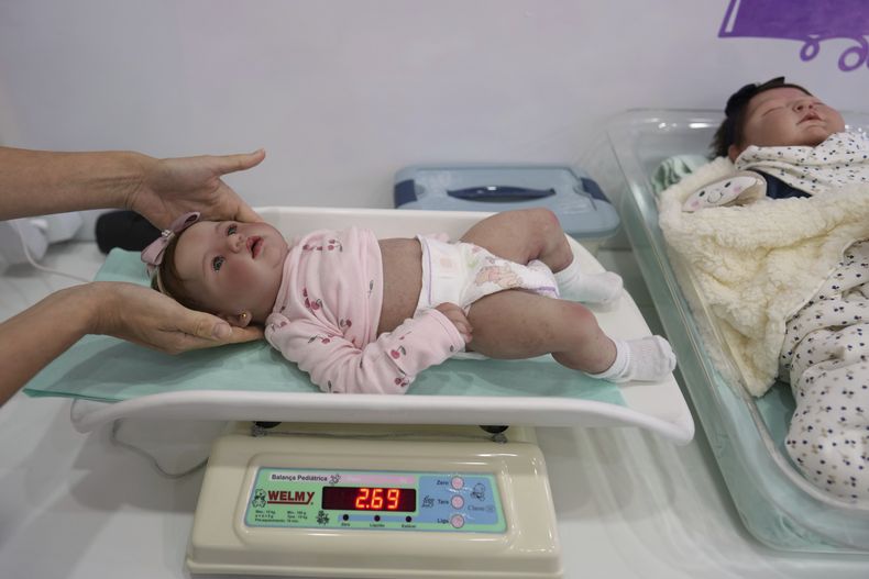 Una empleada pesa a una muñeca hiperrealista reborn en un centro comercial, el sábado 24 de mayo de 2025, en Campinas, Brasil. (AP Foto/André Penner)
