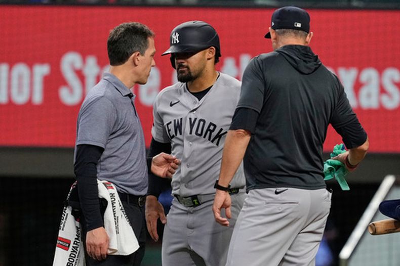 Jasson Domínguez (centro), de los Yankees de Nueva York, habla con un preparador físico del equipo mientras el mánager Aaron Boone (derecha) observa, luego de que Domínguez fuera golpeado por un lanzamiento en la cuarta entrada de un partido de béisbol contra los Rangers de Texas, el miércoles 29 de abril de 2026, en Arlington, Texas. (AP Foto/Tony Gutierrez)