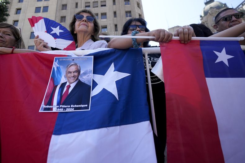 Chilenos se encuentran detrás de una valla afuera del palacio presidencial de La Moneda esperando la llegada del ataúd del expresidente Sebastián Piñera en Santiago, Chile, el viernes 9 de febrero de 2024. El dos veces exmandatario murió el 6 de febrero en un helicóptero al chocar. Tenía 74 años. (AP Foto/Esteban Félix)