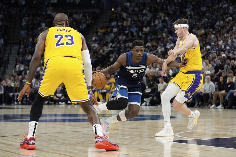 El escolta de los Timberwolves de Minnesota, Anthony Edwards (5), avanza hacia la canasta mientras el alero de los Lakers de Los Ángeles, LeBron James (23), y el escolta Austin Reaves (15), defienden durante la primera mitad del Juego 3 de una serie de playoffs de primera ronda de baloncesto de la NBA, el viernes 25 de abril de 2025, en Minneapolis. (AP Foto/Abbie Parr)