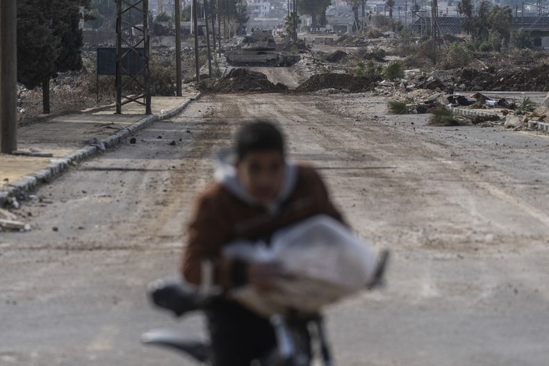 Un niño lleva pan en bicicleta a su casa mientras vehículos blindados del ejército israelí bloquean una carretera que conduce a la ciudad de Quneitra, Siria, el domingo 5 de enero de 2025. (AP foto/Mosaab Elshamy)
