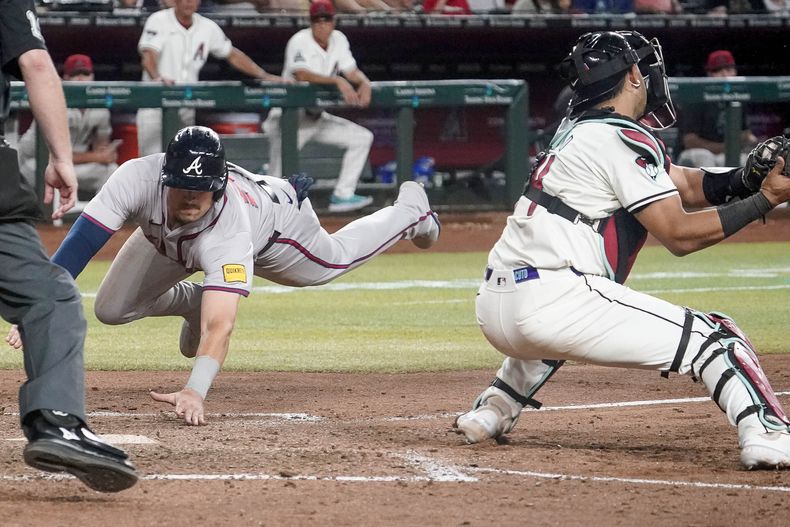 Austin Riley, de los Bravos de Atlanta, se barre de cabeza en el plato mientras que Gabriel Moreno (14), receptor de los Diamondbacks de Arizona, espera la pelota durante la 11ma entrada del juego de béisbol del lunes 8 de julio de 2024, en Phoenix. Los Bravos ganaron 5-4. (AP Foto/Darryl Webb)