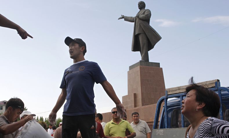 ARCHIVO - Vecinos locales de origen kirguís y uzbeco reciben ayuda humanitaria ante una estatua del fundador de la Unión Soviética, Vladimir Lenin, en una plaza central de la ciudad de Osh, en el centro de Kirguistán, el martes 22 de junio de 2010. (AP Foto/Sergei Grits, Archivo)