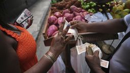 Maite Hernandez, que luce sus uñas arregladas, toma el cambio de un vendedor de verduras en La Habana, Cuba, el sábado 5 de julio de 2025. (AP Foto/Ramon Espinosa)