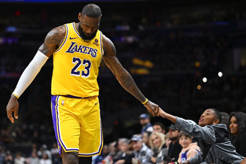 LeBron James, de los Lakers de Los Ángeles, festeja con un fanático, durante el partido del miércoles 3 de abril de 2024, ante los Wizards de Washington (AP Foto/John McDonnell)