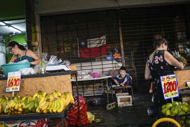 ARCHIVO - Un niño juega con un teléfono celular mientras sus padres colocan un puesto en el mercado popular de La Vega en Santiago, Chile, el 9 de febrero de 2023. La pobreza se redujo en Chile del 10,7% en 2020 al 6,5% in 2022, de acuerdo con un estudio oficial sobre la situación de los hogares difundido el jueves 27 de julio de 2023, en el que también se recoge que la extrema pobreza cayó del 4,5%. al 2,0% en el mismo periodo. (AP Foto/Matías Delacroix, Archivo)