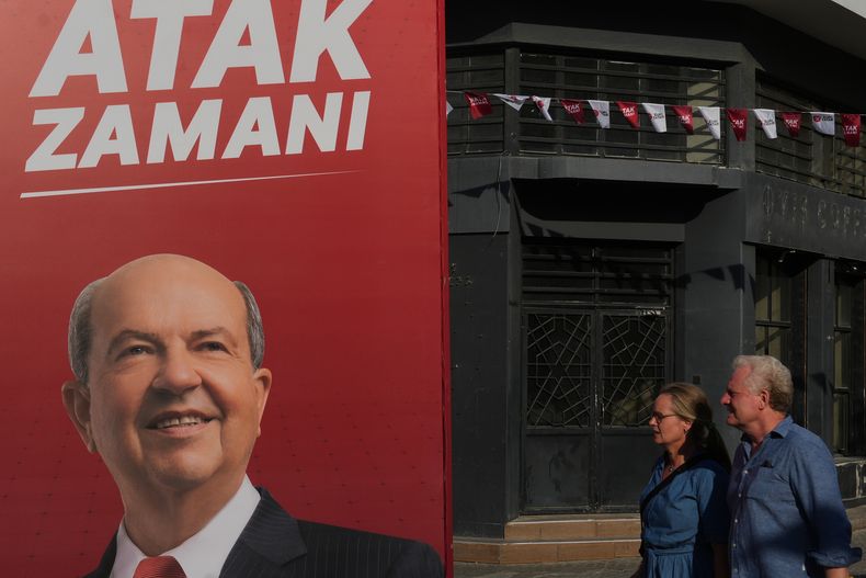 Una pareja camina junto a un cartel de campaña del líder turcochipriota y candidato Ersin Tatar, antes de las elecciones turcochipriotas en la parte norte ocupada por Turquía de la dividida Nicosia, en Chipre, el viernes 17 de octubre de 2025. (AP Foto/Petros Karadjias)