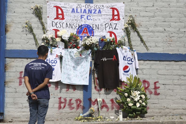 Un aficionado del Alianza se ve parado ante las ofrendas colocadas en memoria de aficionados muertos en una estampida en el estadio Cuscatlán ante el estadio, en San Salvador, El Salvador, el lunes 22 de mayo de 2023. Un juez de San Salvador ordenó que los cinco responsables -tres del club y dos del estadio- permanezcan en prisión preventiva mientras son procesados por el delito infracción a las reglas de seguridad en modalidad agravada. (AP Foto/Salvador Meléndez)