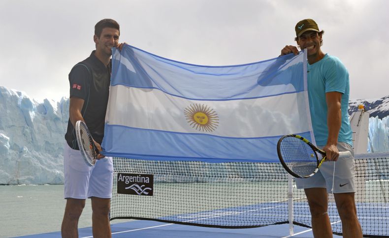En esta fotograf&iacute;a distribuida por el Ministerio de Turismo de Argentina, el tenista espa&ntilde;ol Rafael Nadal (derecha) y el serbio Novak Djokovic sostienen una bandera argentina mientras posan frente al glaciar Perito Moreno desde una cancha de