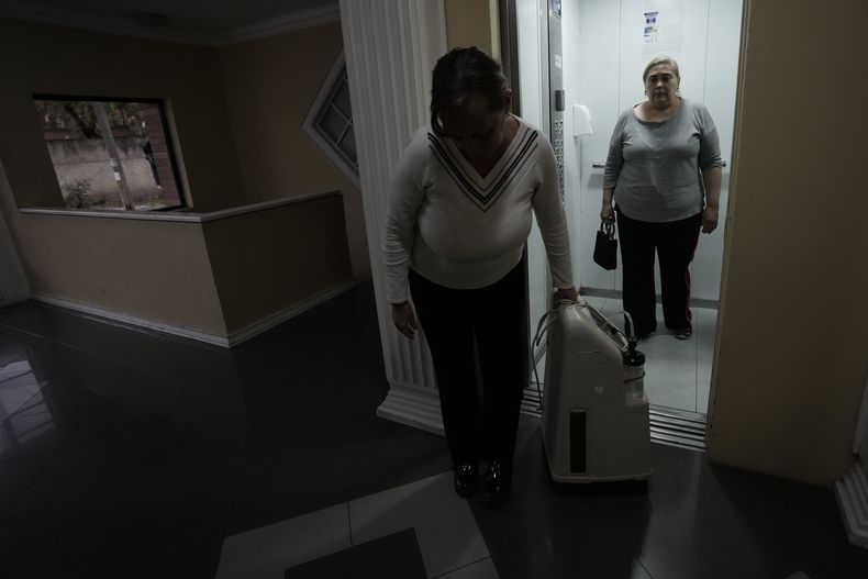 Linda Vidal, paciente con cáncer que depende de un concentrador de oxígeno eléctrico para respirar bien, espera mientras Gabriela saca del ascensor el aparato, ante los cortes de electricidad de hasta 14 horas diarias en el país, debido a una severa sequía, en Quito, Ecuador, el jueves 24 de octubre de 2024. (AP Foto/Dolores Ochoa)