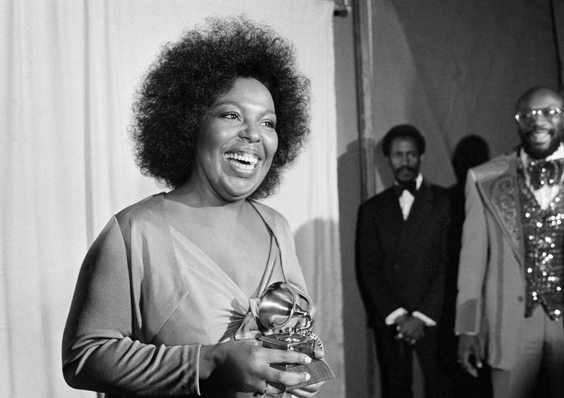ARCHIVO - Roberta Flack sonríe mientras sostiene el premio Grammy que recibió por su álbum Killing Me Softly With His Song ante la mirada del cantante Isaac Hayes, derecha, en la entrega de los premios Grammy en Los Ángeles, el 4 de marzo de 1974. (AP Foto/Harold Filan, archivo)