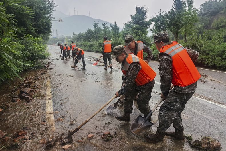 En esta imagen publicada por la agencia de noticias Xinhua, miembros de la Policía Armada Popular China ayudan a despejar un tramo de carretera en el distrito de Miyun, duraante alertas de lluvias, al norte de Beijing, el 27 de julio de 2025. (Wang Xiqing/Xinhua via AP)