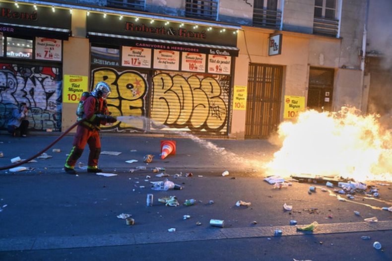 Un bombero extingue un incendio durante enfrentamientos con la policía, un día después de una manifestación contra el aumento del costo de vida —en la que se sumaron las reivindicaciones de los estudiantes—, en París, el domingo 18 de octubre de 2026. (Foto AP/Emma Da Silva)