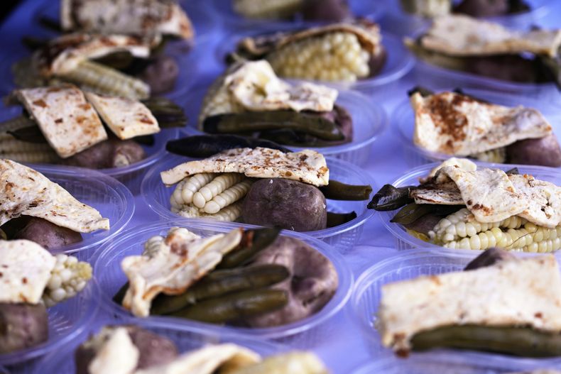 Recipientes con raciones de Plato Paceño se encuentran sobre una mesa mientras los chefs preparan esta comida tradicional con queso, papas, frijoles y maíz, en un evento para los necesitados que celebra el Día de la Independencia de la ciudad de La Paz, Bolivia, el lunes 14 de julio de 2025. (Foto AP/Juan Karita)