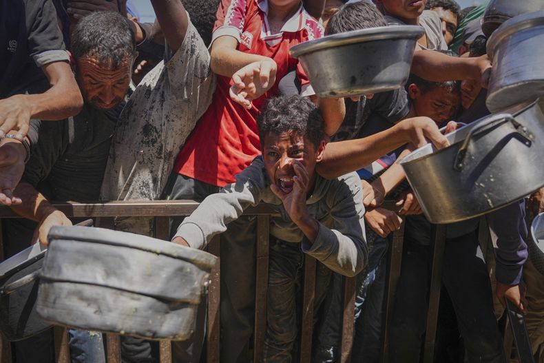Palestinos luchan por recibir comida distribuida en una cocina comunitaria en el área de Muwasi de Jan Yunis, en la Franja de Gaza, el 23 de mayo de 2025. (AP Foto/Abdel Kareem Hana)