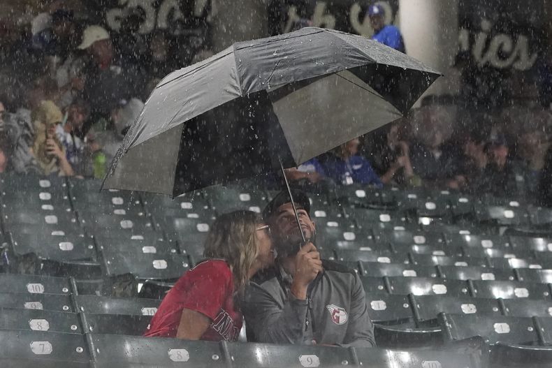 Una pareja de fanáticos se guarece de la lluvia que obligó a suspender el juego del miércoles 23 de agosto de 2023, entre los Dodgers de Los Ángeles y los Guardianes de Cleveland (AP Foto/Sue Ogrocki)