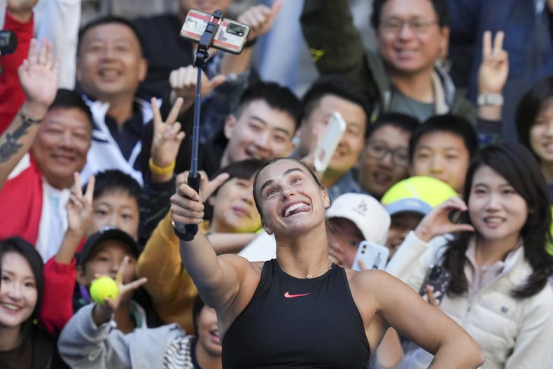 Aryna Sabalenka de Bielorrusia se toma una selfie con los fanáticos después de ganar contra Madison Keys de Estados Unidos durante su partido individual femenino del torneo de tenis Abierto de China, en el Centro Nacional de Tenis en Beijing, el miércoles 2 de octubre de 2024. (AP Foto/Achmad Ibrahim)