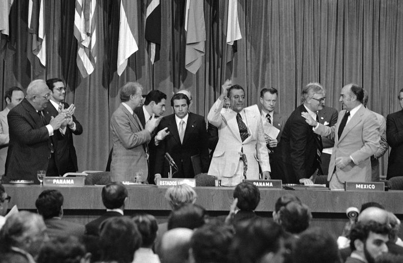 ARCHIVO - El presidente Jimmy Carter aplaude y el general Omar Torrijos saluda después de la firma e intercambio de tratados en la ciudad de Panamá el 16 de junio de 1978, que dieron el control del Canal de Panamá al país centroamericano. En el extremo derecho está Zbigniew Brzezinski, asesor de seguridad nacional de Carter. (AP Foto, Archivo)